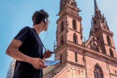 Junger Mensch mit Kopfhörer schaut den Münster an. Er nimmt an die MyClimate Audio Adventure teil.